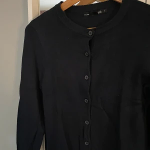 Svart kofta från 157 med knappar - En klassisk svart kofta från 157 med rund halsringning och knäppning framtill. Långärmad och i mjukt material som passar perfekt till lager-på-lager. Enkel och stilren design som funkar till det mesta. Står ej för postens slarv Köpt är köpt, gär ej att returneras. Pris går att diskuteras