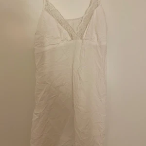 Vit kort nattlinne med spetsdetaljer - Söt vitt kort nattlinne med smala axelband och v-ringning dekorerad med spets. 