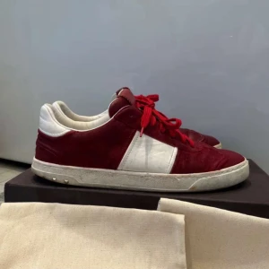 Valentino flycrew sneakers röd/vit - Snygga Valentino Rockrunner sneakers i rött och vitt skinn med röda snören och coola nitar på hälen. Klassisk låg modell med vit sula och rund tå. Perfekta för dig som vill sticka ut med exklusiva detaljer och streetkänsla.