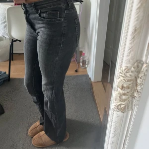 svart/grå bootcut jeans med slits, midwaist - Säljer ett par svarta bootcut jeans med råa, fransiga benslut och slits nertill. Jeansen har hög midja, klassisk femficksmodell och är i stretchigt denimtyg. Snygg tvätt med lite slitningar för en cool look.