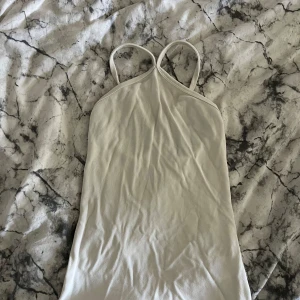 Vit ribbad linnetopp med smala band - Säljer en stilren vit linnetopp med smala axelband som korsas i ryggen. Toppen är ribbad och har en enkel, clean look som passar perfekt till jeans eller kjol. Materialet är mjukt och stretchigt för en bekväm passform.