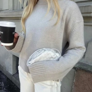 Beige stickad tröja - Säljer en stilren beige kashmir stickad tröja med ribbade detaljer vid ärmslut och nederkant. Tröjan har en avslappnad passform och långa ärmar, perfekt för kyligare dagar. Lite nopprig men ska avkopplas med maskin innan leverans! 