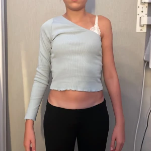 Ljusblå ribbad oneshoulder topp - Säljer en ljusblå ribbad topp från Bik Bok med oneshoulder-design och lång ärm på ena sidan. Toppen är croppad med vågig kant nertill och har en tight passform. Perfekt för dig som vill sticka ut med en unik och trendig look.