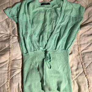 Mintgrön topp från Vero Moda - Superfin mintgrön topp från Vero Moda med knyt i midjan. Toppen har korta ärmar och är stickad i ett lätt, luftigt material med små hål för extra detalj. Perfekt för dig som gillar en fräsch och somrig look! Storleken är m men jag skulle säga att den sitter som S