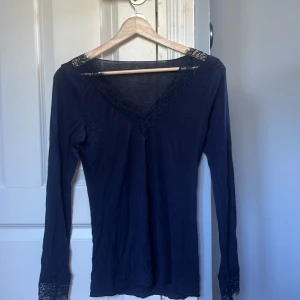 Mörkblå spetsblus från Intimissimi - Supersnygg mörkblå långärmad blus från Intimissimi med v-ringning och spetsdetaljer vid halsringning och ärmslut. Tunn och mjuk i bomullsmix, perfekt för lager-på-lager eller som statement-piece. Sitter figurnära och har en feminin vibe.
