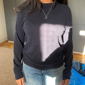 Mörkblå stickad tröja med rund hals - Enkel och stilren mörkblå chasmire  tröja med rund halsringning och långa ärmar. Tröjan har en klassisk passform och ribbade muddar vid ärmslut och nederkant. Perfekt att matcha med jeans för en clean look.