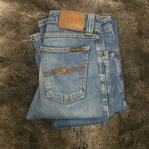 Nudie Jeans - Säljer ett par klassiska blå jeans från nudie jeans. Jeansen har snygga kontrastsömmar, fem fickor och Nudie-logga på bakfickan. Perfekta för dig som gillar en stilren look. Storleken är 27/34 och passar dig som är ungefär 160-168 beror på hur du vill passformen ska vara! Kom med bud och frågor!