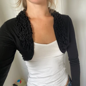 Bolero med volangkant - Säljer en svart boleroväst med långa ärmar och snygga volangdetaljer längs hela kanten.