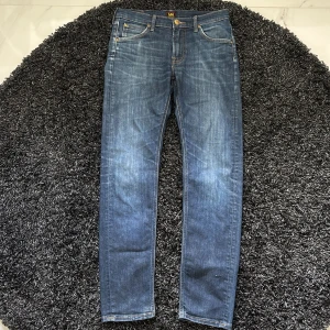 Blå raka jeans från Lee - Snygga blå jeans från Lee med klassisk femficksdesign och raka ben. Jeansen har en lätt tvättad look och subtila slitningar för en avslappnad vibe. Tillverkade i mjukt denimtyg som sitter skönt hela dagen. Jag är 181 cm.