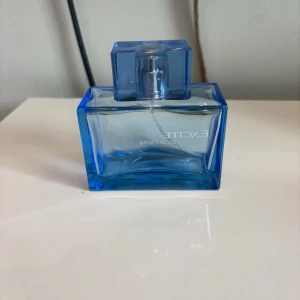 Excite by Oriflame parfym blå (tom flaska) - Fräsch parfym från Oriflame, Excite, i en stilren blå glasflaska med rektangulär form och matchande blått lock. Flaskan har en modern design och känns riktigt clean på hyllan. Perfekt för dig som gillar fräscha dofter och snygg förpackning.