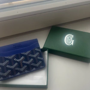 Blå Goyard plånbok/korthållare - Säljer en blå plånbok från Goyard med deras ikoniska grafiska mönster i vitt och svart. Plånboken är i smidig modell med flera kortfack och har en lyxig känsla tack vare det exklusiva materialet och designen. Perfekt för dig som vill ha något unikt och stilrent.