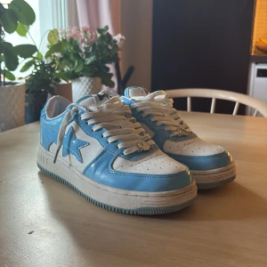 BAPE STA sneakers i blått och vitt - Snygga BAPE STA sneakers storlek 42 men passar 43 i blankt blått och vitt skinn med klassisk stjärndesign på sidan. Låga med vit sula, perforerad tå och vita snören med metall-detalj. Perfekta för dig som vill sticka ut med streetwear-vibe.