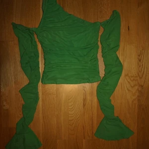 Grön one shoulder topp med volangärm - Säljer en grön, tight och croppad topp med one shoulder-design och långa, rynkade ärmar som avslutas med volang. Toppens material är stretchigt och lätt, perfekt för dig som vill sticka ut med en cool och unik look.