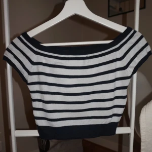 Randig offshoulder topp - Snygg croppad topp med marinblå och vita ränder. Offshoulder-modell med korta ärmar och bred ribbad kant upptill och nedtill. Perfekt för en trendig och avslappnad look.