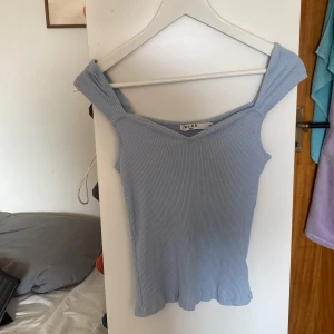 Ljusblå topp - Supersöt ljusblå ribbad topp från NA-KD med breda axelband och v-ringning. Toppen är ärmlös och har en figurnära passform som ger en snygg siluett. Perfekt att styla med jeans eller kjol för en fräsch look.