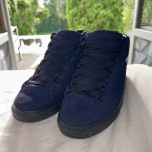 Mörkblåa suede balenciaga arena - Säljer dessa sjukt snygga Balenciaga Arena High Sneakers i en djup mörkblå mocka, superrena och riktigt svåra att få tag på.  Storlek EU 40, men passar mer som en 42 (innersula mäter 27 cm). De är i fint skick och har bara använts ett fåtal gånger. Dock finns lite slitage på hälen och snörena på högra skon är lite slitna som syns på sista bilden, min hund blev tyvärr sugen på snören 💔😢  Nästan som nya Sällsynt färg Snygg och unik modell  Hör av dig om du har några frågor!
