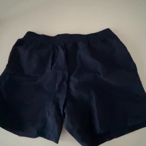 Mörkblåa badshorts från SOC - Mörkblåa badshorts från SOC med vit snörning i midjan. De har en loose passform och elastisk midja för extra komfort. 