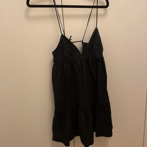 Zara klänning - Supersöt svart kort klänning med tunna axelband och v-ringning. Klänningen har volang nertill och knytning i ryggen. Storlek s