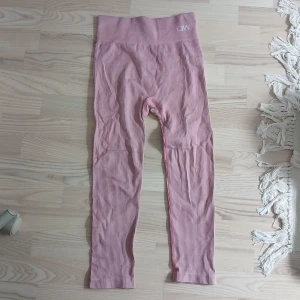 Rosa ribbade leggings från ICANIWILL - Säljer ett par ljusrosa ribbade leggings från ICANIWILL. De har hög midja och är tillverkade i ett stretchigt material med 76% polyamid och 16% elastan. Perfekta för träning eller chill, med snygg passform och diskret logga i midjan.