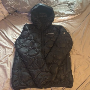 Svart dunjacka Peak Performance S - Svart dunjacka från Peak Performance i storlek S. Jackan har huva, dragkedja framtill och quiltad design. Perfekt för kalla dagar med sin fluffiga och varma känsla. Snygg och enkel att matcha med allt. Nypris ca 3000kr kom med frågor och prisförslag 