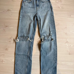 Blå slitna jeans från ginatricot  - Blå jeans med raka ben och slitningar över knäna från ginatricot. Klassisk femficksmodell med normal passform och hög midja. 