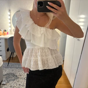 Vit omlott volang topp från Zara - Superfin vit topp med volanger och broderade spetsdetaljer. One shoulder-modell med omlottkänsla och flera lager volang nertill. 