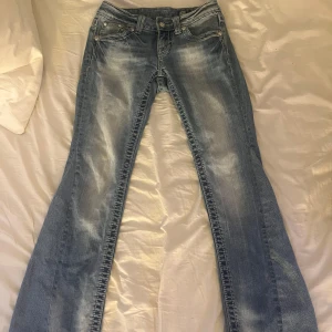 Miss Me bootcut jeans ljusblå, strl 25 - Snygga ljusblå bootcut jeans från Miss Me med dekorativa nitar på fickorna. Klassisk femficksmodell med tydliga kontrastsömmar och coolt lädermärke bak. Perfekta för dig som gillar en avslappnad men trendig look. Byxorna är före detta skinny men professionellt omsydda till bootcut!