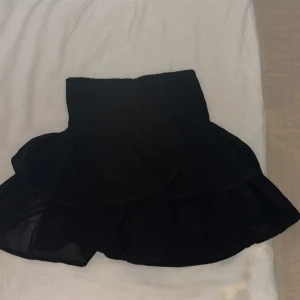 Svart volangkjol med resårmidja - Supersöt svart kortkjol med volanger och bred resår i midjan. Kjolen har en luftig och flowy känsla. Passar  till crop tops eller oversized hoodies. 