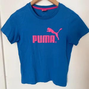 Blå Puma t-shirt med rosa logga - Blå t-shirt från Puma med stor rosa logga framtill och liten logga bak i nacken💙