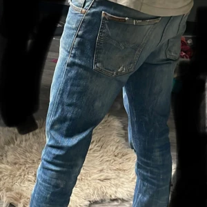 Blå Replay jeans med slitningar - Säljer ett par blå Replay jeans med snygga slitningar och tvättade detaljer. Jeansen har klassisk femficksdesign, normal passform och raka ben. Perfekta för dig som gillar en avslappnad och trendig look.