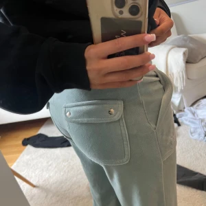Ljusgröna mjukisbyxor Juicy Couture - Snygga ljusgröna mjukisbyxor från Juicy Couture med bred resår i midjan och snörning. Jag andvänder inte dom längre för att dom är lite för små❤️Byxorna har stora fickor fram och bak med lock och silverfärgade knappar. Mjukt material som känns skönt mot huden, perfekt för chill dagar. Jag har andvänt dom några gånger🥰