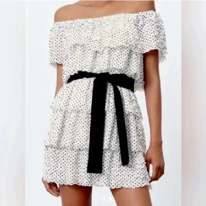 Prickig kortklänning från Zara - Supersöt vit kortklänning med svarta prickar från Zara. Offshoulder-modell med volanger och svart knytband i midjan. Populär och eftertraktad som inte går att få tag på längre , den är aldrig använd därav inga defekter och i nyskick☺️