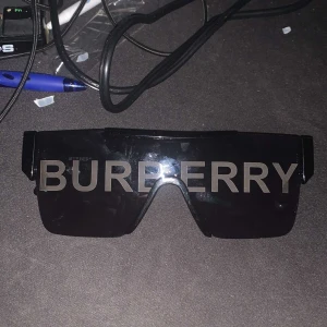 Svarta Burberry shield-solglasögon - Säljer ett par svarta shield-solglasögon från Burberry med stor logga över hela linsen. Behöver de inte längre fick de som en present från min kusin de är i mycket bra skick och vill helst ha 475kr men priset kan diskuteras 