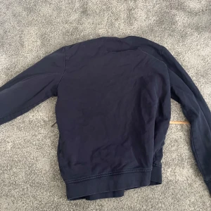 Mörkblå sweatshirt från 157 - En basic mörkblå sweatshirt från 157 med rund halsringning och långa ärmar. Tröjan är i mjuk bomull och har ribbade muddar vid ärmslut och nederkant. Perfekt för en chill och avslappnad stil.