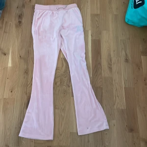 Ljusrosa velourbyxor med strassdetalj - Supermjuka ljusrosa velourbyxor med bootcut och snörning i midjan. Byxorna har två bakfickor och en snygg strassdetalj framtill. Perfekta för en chill och trendig look.