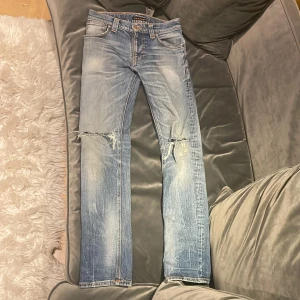 Nudie jeans  - Tjena ! Säljer ett par ljusblå jeans med en unik tvätt från Nudie med slitningar och hål på knäna. Klassisk femficksmodell med orangea sömmar och Nudie-logga på bakfickan. Jeansen har rak passform. Jeansens ena ficka har ett hål och ett hål under gylfen annars är dom i ett fint skick. (Storlek w28,l32) Kontakta vid intresse eller fler bilder 🙌 