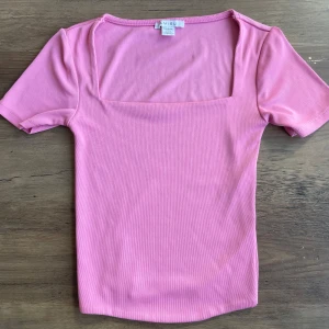 Rosa ribbad topp från Amisu - Supersöt rosa topp från Amisu med fyrkantig ringning och korta ärmar. Den är ribbad och har en tight passform som sitter snyggt på kroppen. Perfekt att styla med jeans eller kjol för en fräsch look.