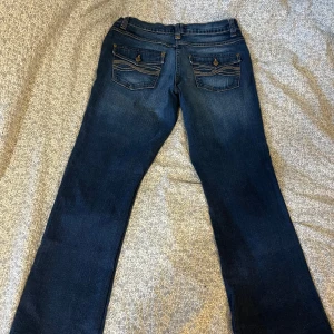 Vintage bootcut-jeans - Så fina bootcut-jeans från märket ElleNor. Jättefina fickor med knapp och broderi. Storlek 36. Fint skick förutom en liten vit fläck på framsidan och en annan liten fläck på baksidan (syns på bilderna)