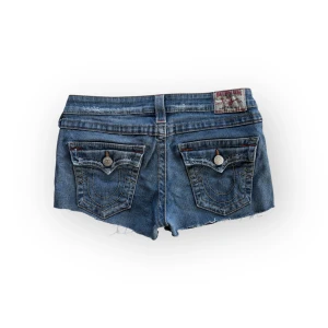 True Religion jeansshorts blå - Snygga blå jeansshorts från True Religion med råa kanter (avklippta)  och klassiska bakfickor med dekorativa sömmar. Midja 39, fråga gärna om fler mått 💗Storlek W29 passar S-M