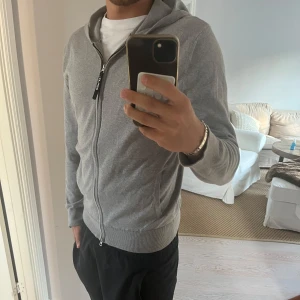 Replay tröja - Säljer en stilren grå hoodie från Replay med hel dragkedja och huva. Tröjan har ribbade muddar, två fickor framtill och en snygg Replay-detalj på dragkedjan. Perfekt för chill dagar eller när du vill ha en enkel look. Personen på bilden är 180, köpt för 1000kr!