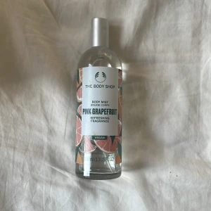 The Body Shop Pink Grapefruit Body Mist - Fräsch body mist med doft av pink grapefruit från The Body Shop. Kommer i en genomskinlig glasflaska med silverfärgad spraykork och färgglad etikett med grapefruktmotiv. Vegansk formula och 100 ml storlek – perfekt för dig som gillar fruktiga och uppiggande dofter.