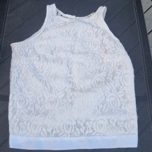 Vit spetsblus med rosett i ryggen - Superfin vit blus i spets med blommigt mönster och bred rosett i ryggen. Ärmlös modell med rund halsringning och snygg öppning bak. Perfekt för dig som gillar romantiska detaljer och vill sticka ut lite extra. Står ingen storlek men skulle säga S-M.