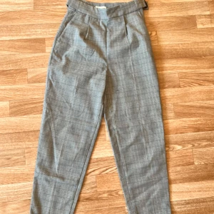 Grå rutiga kostymbyxor - Snygga grå kostymbyxor med rutigt mönster och hög midja. Byxorna har avsmalnande ben och klassisk passform, perfekta till en stilren look. Tillverkade i ett mjukt tyg som känns bekvämt hela dagen.