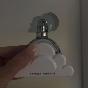 Ariana Grande Cloud parfym - Superfin parfym från Ariana Grande i modellen Cloud. Flaskan är rund och transparent med en blå ton och har ett unikt lock i form av ett moln. Parfymen kommer med en vit molnformad bas och silvriga detaljer. Perfekt för dig som gillar söta och fräscha dofter.