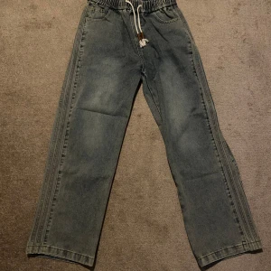 Ljusblåa japanska jeans med snörning - Ett par avslappnade jeans med resår i midjan och dragsko. Jeansen har en bredare passform och sidoränder längs benen. Är baggy på mig som är 185 cm lång. Knappt använda, 3 gånger.