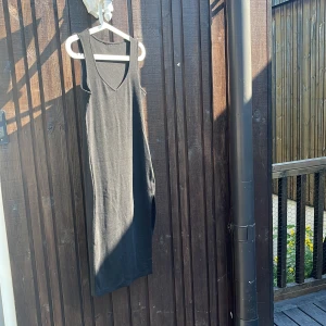 Svart ribbad långklänning med slits - En svart, ärmlös långklänning i ribbat material med v-ringning och slits på sidan. Klänningen har en enkel och stilren design som passar perfekt för sommardagar. Mjuk och stretchig känsla för en bekväm passform.