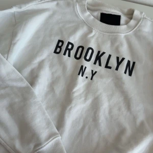Vit sweatshirt  - Vit sweatshirt från lager 157 i storlek XS med svart text BROOKLYN N.Y framtill. Klassisk rund halsringning och långa ärmar. Mjuk insida och ribbade muddar vid ärmslut och nederkant. Har aldrig använt den, Ord pris 200kr. Pris kan diskuteras.
