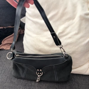 Svart axelväska med kedjedetalj - Snygg vintage svart axelväska i en mix av skinn och bomullstyg (inte äkta skinn). Väskan har silvrig dragkedja upptill, dekorativa sömmar och en snygg kedjedetalj framtill. Och liten ficka inuti väskan på ena sidan och amdra sidan inuti väskan är det en ficka med en liten dragkedja .