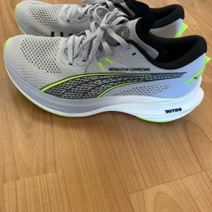 Puma Hyrox Nitro sneakers grå/gul - Snygga Puma Hyrox Nitro sneakers i ljusgrå mesh med svarta och neongula detaljer. Skorna har vit och neongul sula, svart innersida och texten 'NEVER STOP COMPETING' på sidan. Perfekta för träning och löpning, med skön passform och modern look. Har tyvärr inte skoboxen kvar, därav priset 