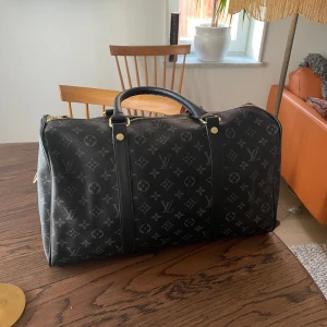 Louis Vuitton bag - Säljer en lyxig svart resväska från Louis Vuitton med klassiskt monogrammönster. Väskan har guldfärgade detaljer, dubbla handtag och dragkedja. Tillverkad i skinn och rymmer allt du behöver för en weekend. Perfekt för dig som vill resa med stil.